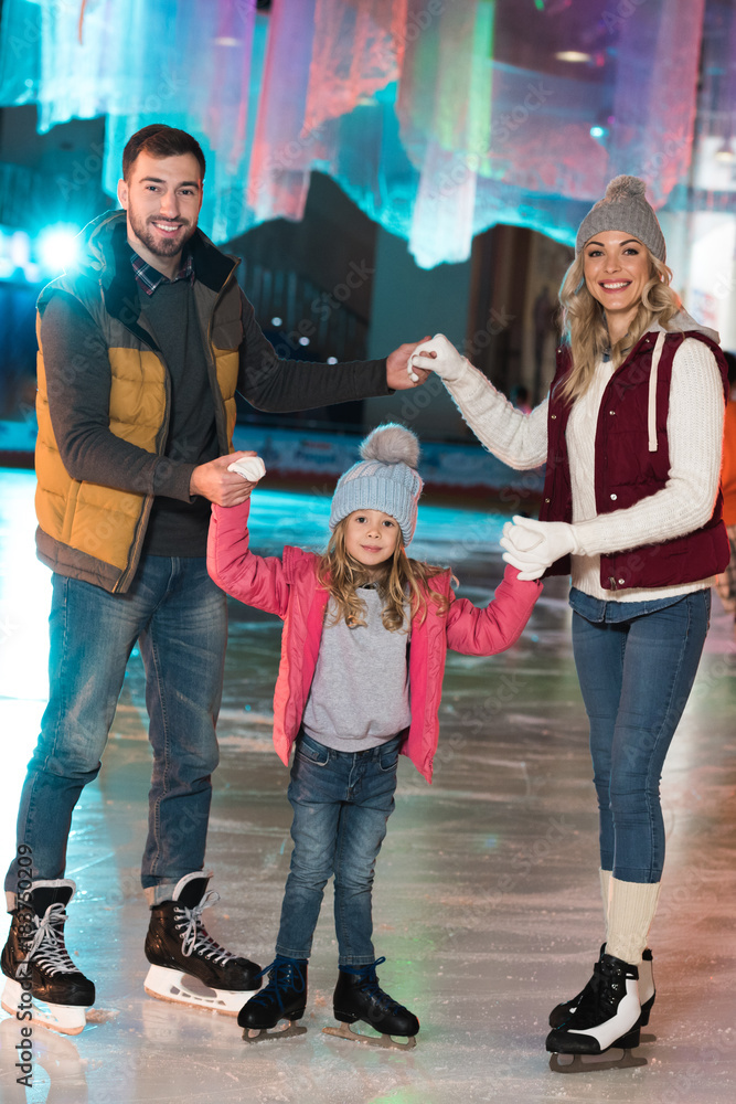 Obraz premium happy young family holding hands and smiling at camera on skating rink