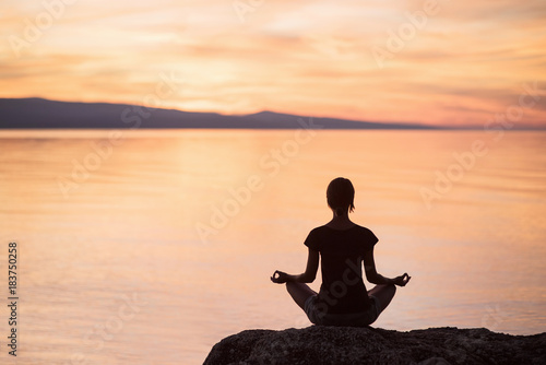 Young woman practicing yoga near the sea at sunset. Harmony and meditation concept. Healthy lifestyle
