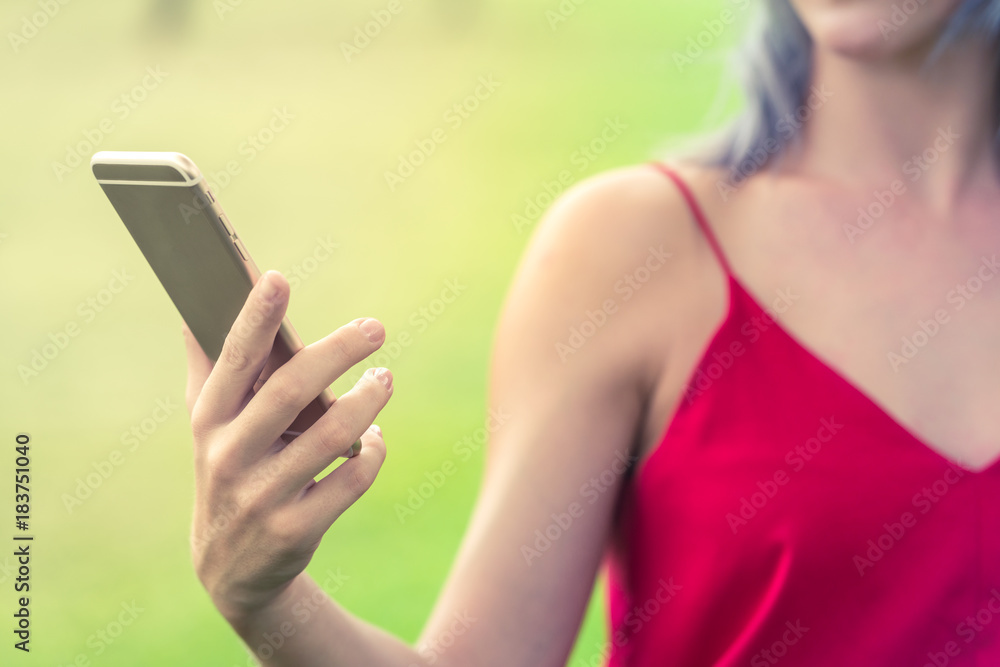 Woman with red shirt holding a smart phone. Blurred green background