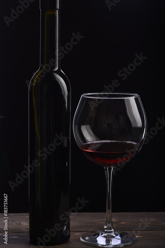 Bottle of wine near glass on black background