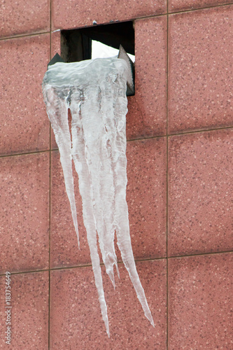 Large stuck together icicle on the exhaust window on a brownish pink tiled wall photo