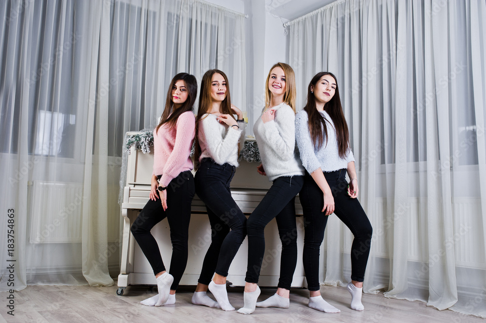 Fototapeta premium Four cute friends girls wear on warm sweaters and black pants against old piano with christmas decoration at white room.