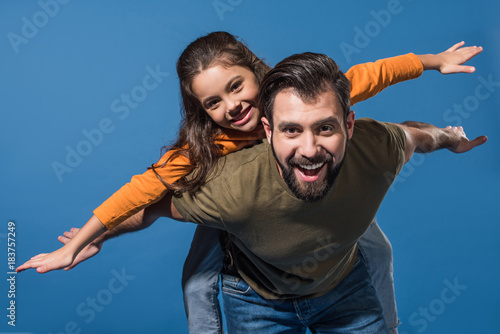father giving piggyback to daughter on blue
