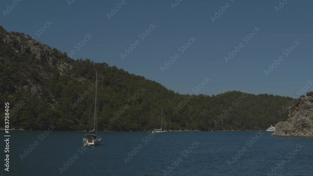 Large and small ships sail through the calm sea between the green hills on warm, sunny summer day Large and small ships sail through the calm sea between the green hills on warm, sunny summer day