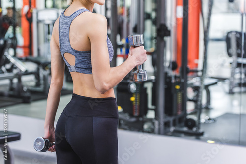 cropped shot of sportive woman working out with dumbbells at gym