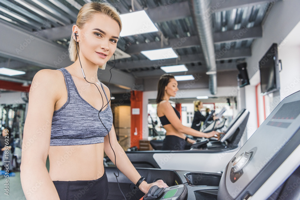 attractive sportive woman running on treadmill at gym with earphones