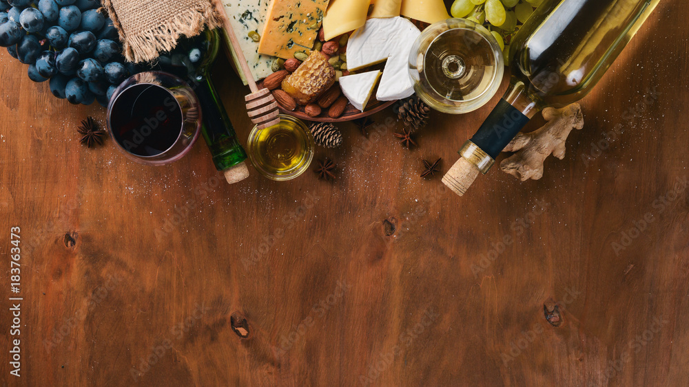 A bottle of wine, and a large assortment of cheeses, honey, nuts and spices, on a wooden table. Top view. Free space for text. - obrazy, fototapety, plakaty 