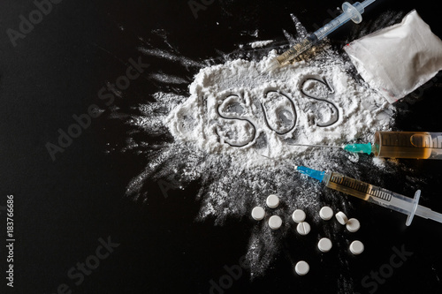 Narcotics heroin, syringes, money on a dark background with the inscription sos and copy space, the concept of crime and drug addiction