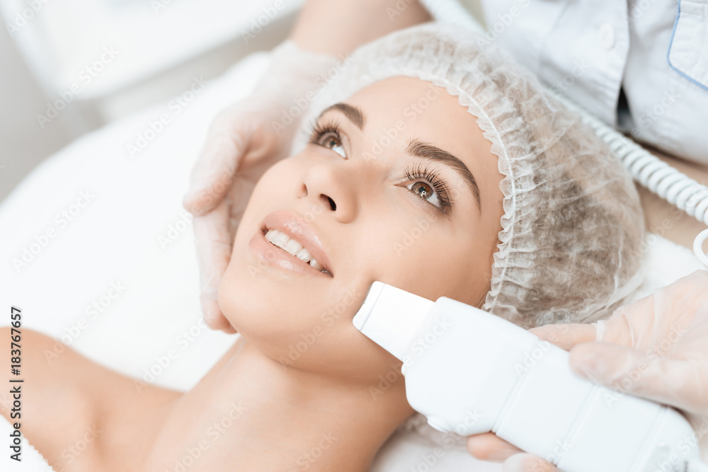 The doctor cleanses the woman's skin with a special medical device. The woman came to procedure of laser hair removal.