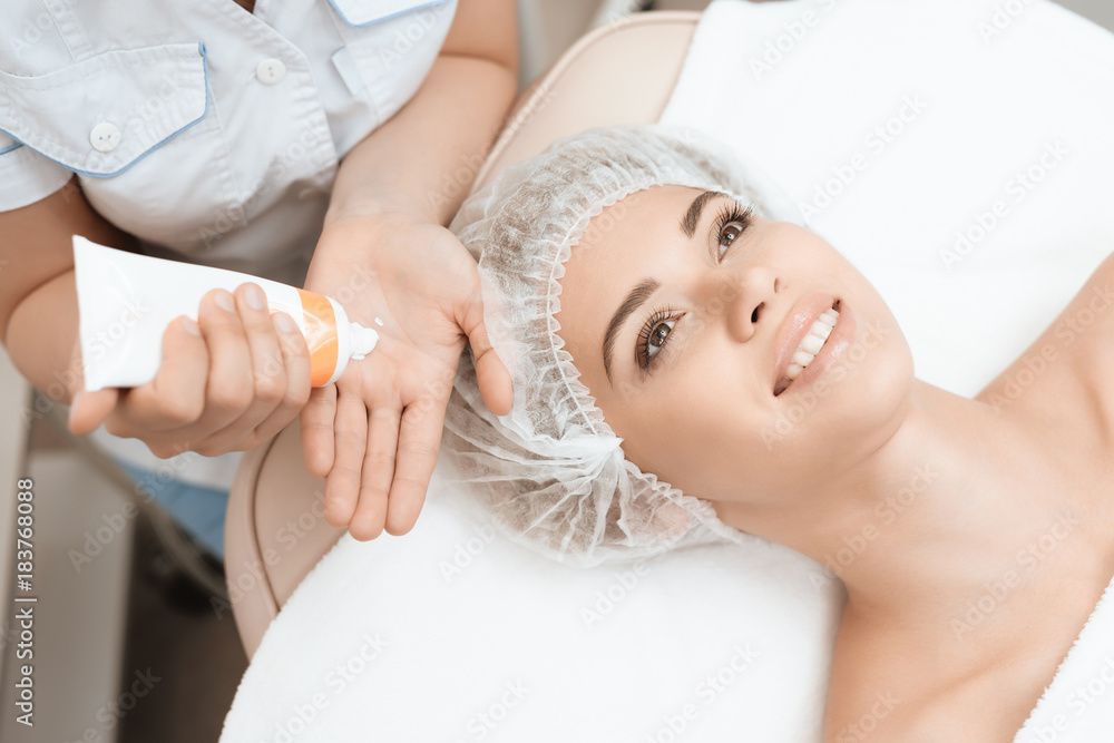 Fototapeta premium Doctor puts on hands a special cream for massage. She treats the skin of face of the girl who came to the beauty salon.