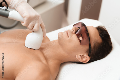 The man came to the procedure of laser hair removal. The doctor treats his neck and face with a special apparatus. photo