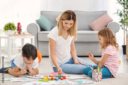 Mother with children painting while sitting on floor indoors