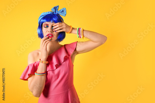 Young woman with rainbow makeup and blue hair on yellow background