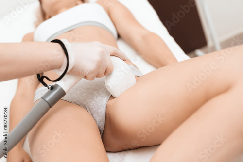 The woman came to the procedure of laser hair removal. The doctor is treating her leg with a device.