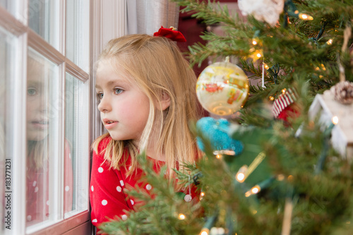 Fotografija beautiful young school age girl looking out window waiting for Santa on Christma