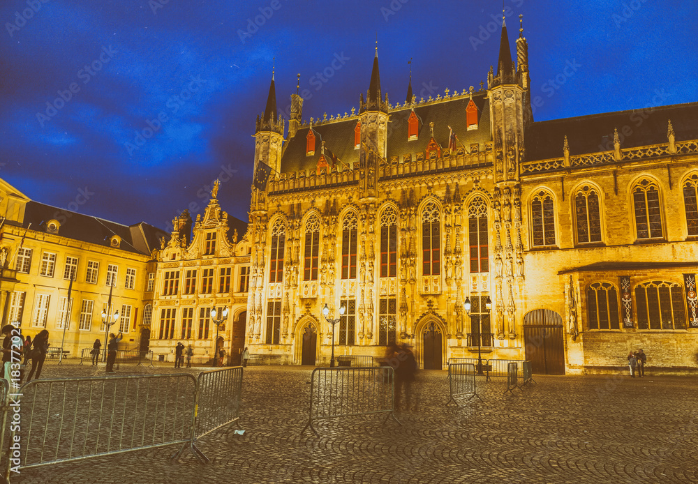 BRUGES, BELGIUM - MARCH 2015: Tourists visit ancient medieval Burg Square at night. Brugge attracts more than 2 million people annually
