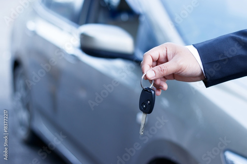 Business man holding car keys with car on background.