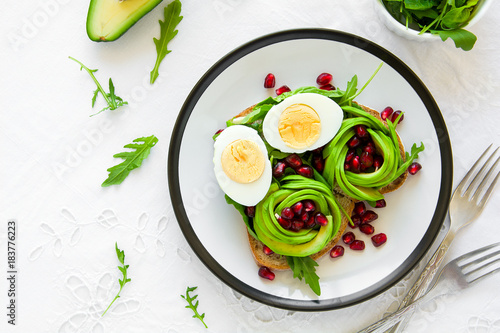 Toast with avocado rose, boiled egg and fresh salad on white table cloth