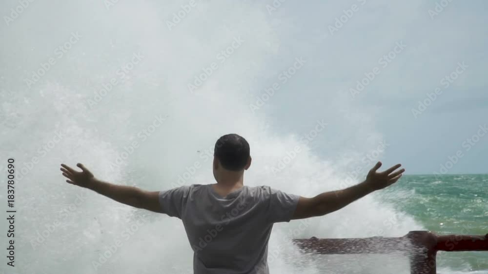 Young Man with Raised Hands Infront of Giant Sea Waves. Slow Motion Young Man with Raised Hands Infront of Giant Sea Waves. Slow Motion