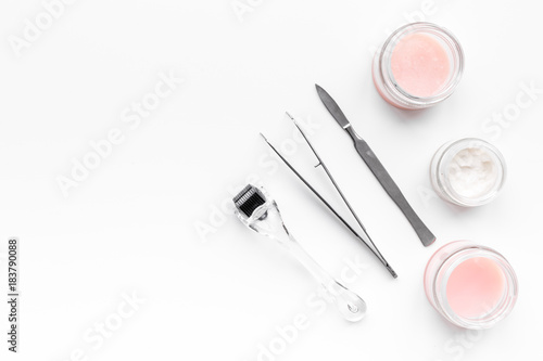 Desk of cosmetoligist. Dermaroller, creams and mask, tools on white background top view copyspace
