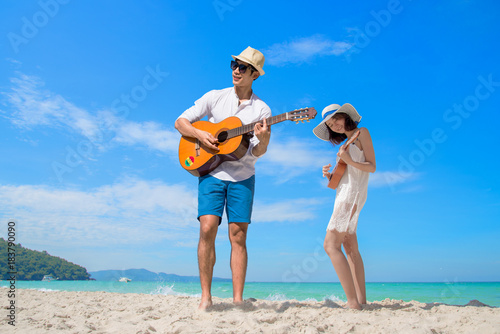 couple lovers in romantice honeymoon playing guitar together on the sea beach in daylight and blue cleared sky in background