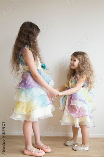Two little girls hold hands and dance together.