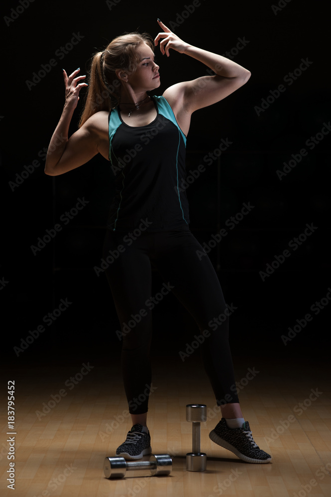 Fit sporty woman showing her muscles, posing on black background. Fitness and sports concept.