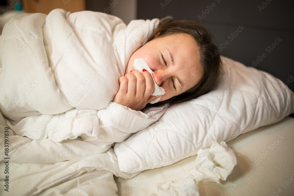 Pretty young brunette woman lying in the bed with handkerchief, looking sick and exhausted