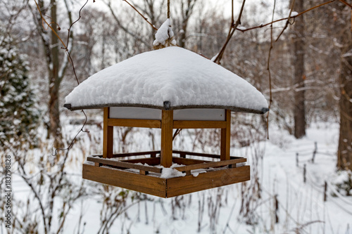 Wooden bird feeder in the snow-covered winter city park
