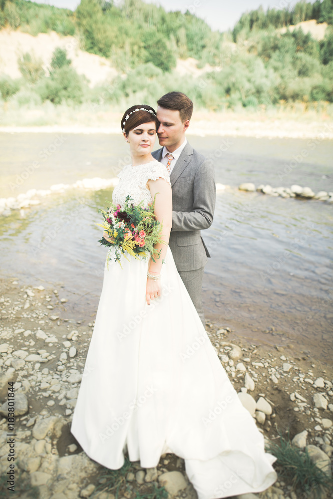 Elegant gentle stylish groom and bride near river with stones. Wedding couple in love Elegant gentle stylish groom and bride near river with stones. Wedding couple in love