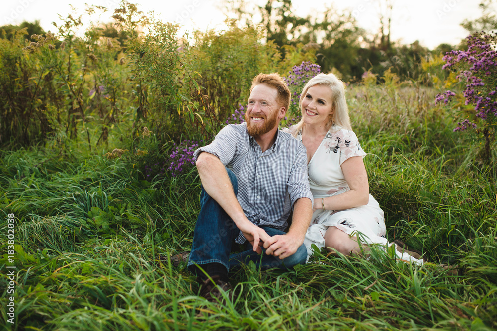 © Connect Images - Couple sitting in tall grass looking away smiling