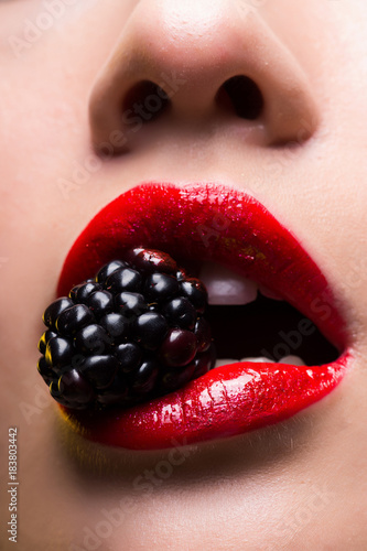 Closeup photo of red female lips with blackberry in teeth
