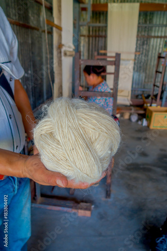 Close up of a man holding in his hand a piece of wool to work on loom manufacturing whool shawl clothing in Nepal photo