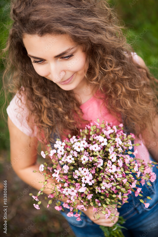 Beautiful curly woman with pink flowers looking down and smile Beautiful curly woman with pink flowers looking down and smile