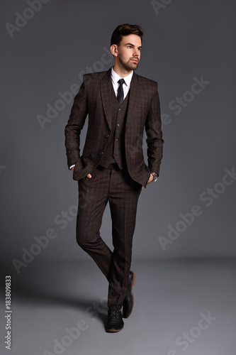 Handsome man in suit is possing and look aside on gray background at studio