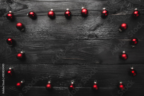 Upper, top, view from above, of evergreen red toys and white Merry Christmas inscription, on black wooden background, with space for text writing, greeting.