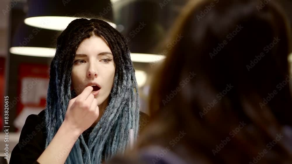 a girl with blue dreadlocks eats in the company of her girlfriend, a teenager is eating French fries a girl with blue dreadlocks eats in the company of her girlfriend, a teenager is eating French fries