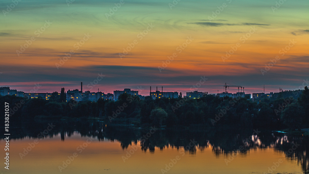 Beautiful sunset skyline of a city and trees with a lake in the foreground