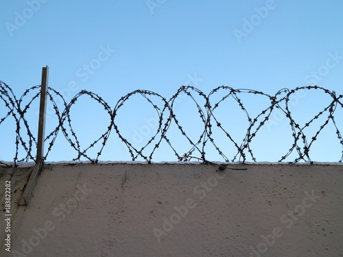 Gray fence with barbed wire in the background of a blue sky with clouds