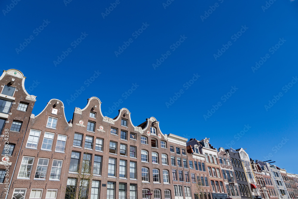 Historical Amsterdam canal houses in a blue sky.