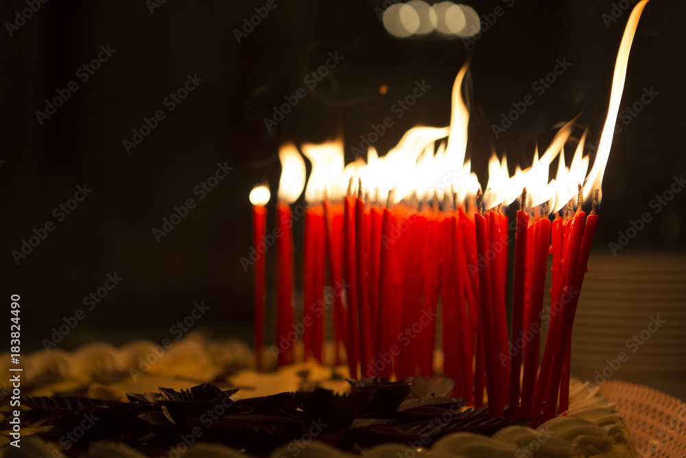 Candles lit on top of a birthday cake, background is a dark room Stock