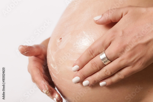 Pregnant woman applying moisturizer on belly, preventing pregnancy stretch marks