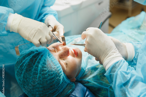 Male old professional dentist surgeon in uniform and female assistant helps to performing operation install dental implant teeth of woman patient in clinic light office with modern tools equipment. photo