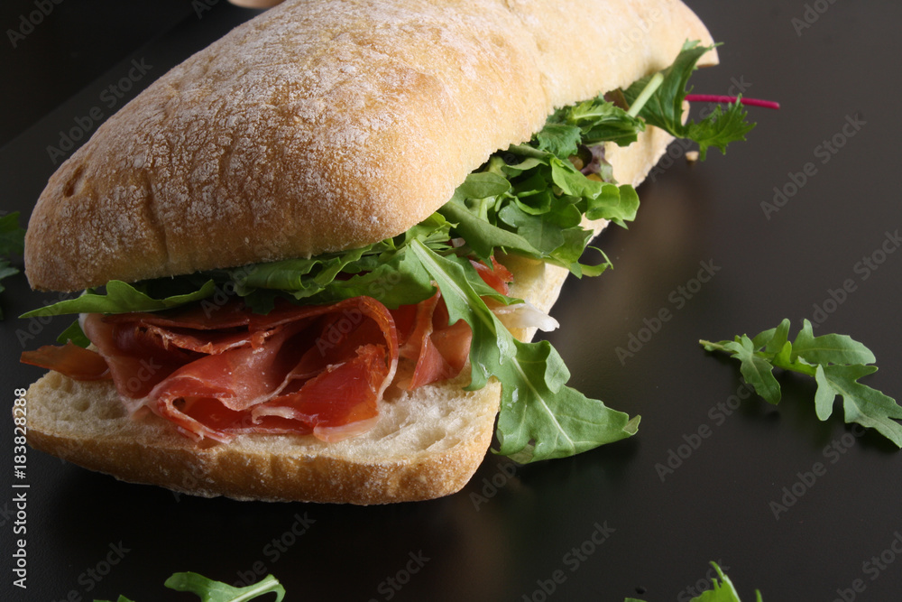 Φωτογραφία Ciabatta sandwich with jamon ham serrano paleta iberica, arugula, rosemary on st