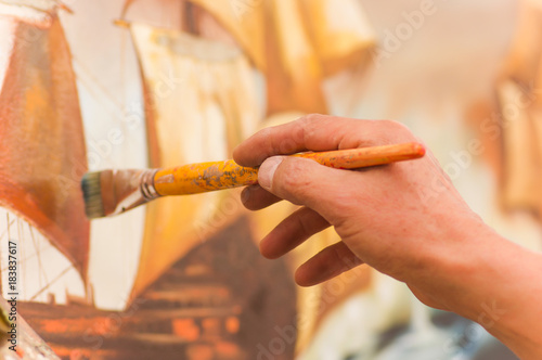 Close up of man hand husing a paint brush over a color palette in art studio, in a blurred background