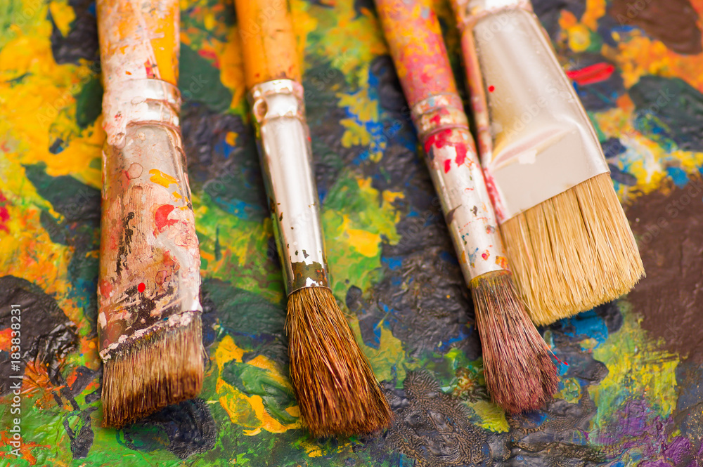 Fototapeta premium Top view of paint brushes over a color palette in a blurred background