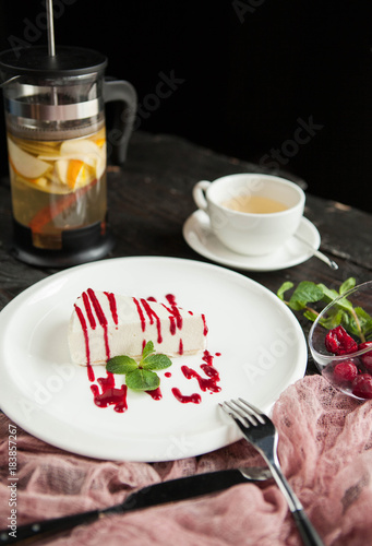 Cheesecake with berry sauce and French press and a cup of tea on a wooden background