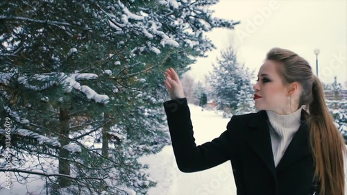 Close-up of Brunette fashionable sexy pretty rich woman or glamour model girl with beautiful long Brunette hair in black coat posing for camera on background of Christmas tree with snow-covered photo