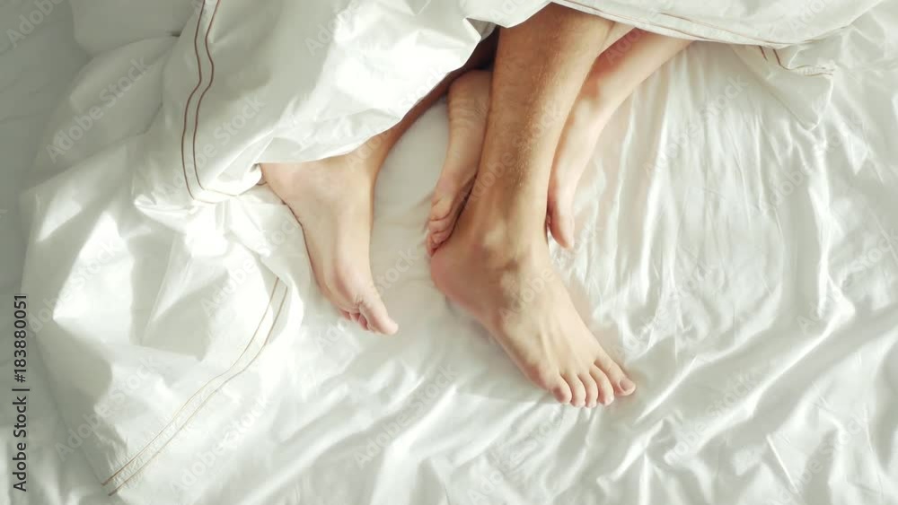 couple in bed making love. male and female legs top view, white linens