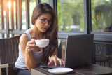 Young casual business woman working on laptop holding coffee cup in outdoor cafe. girl using notebook with concentrate feeling. lady freelance lifestyle.